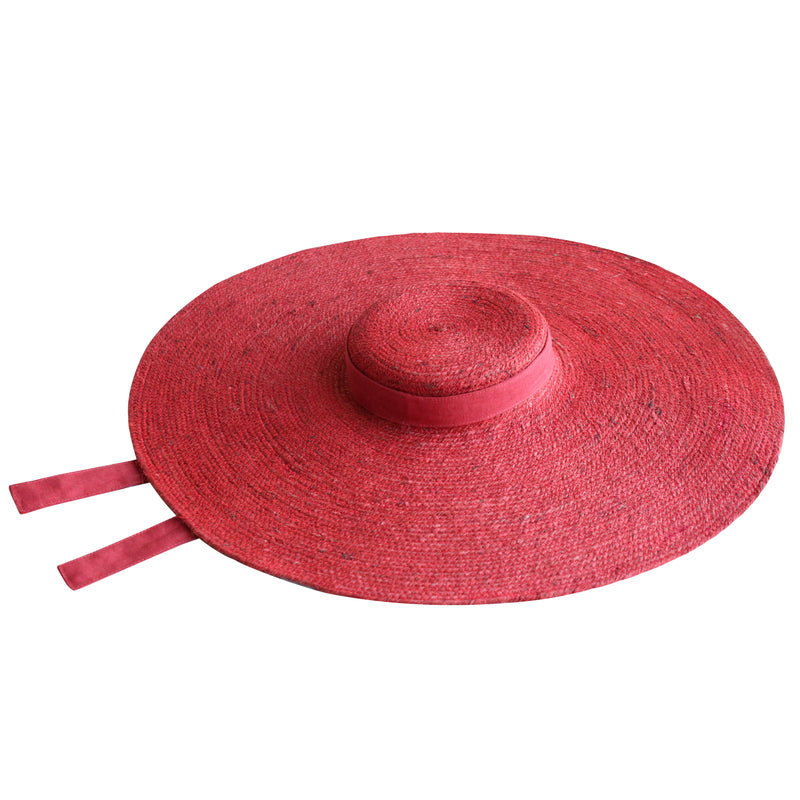 BrunnaCo Lola Wide Brim Jute Straw Hat in Red. A wide-brimmed straw hat in a vibrant red color. The hat is made from natural jute fibers and features a comfortable inner lining. It is perfect for sun protection and style. Handmade by women artisans in Bali, Indonesia