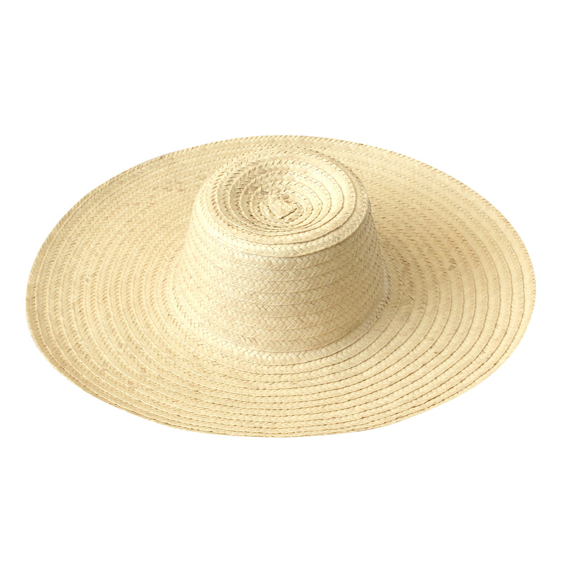 A woman is wearing BrunnaCo Rianna Straw hat made from locally harvested palm straw in Bali. This versatila hat is perfect for a day at the beach or a stroll around town on a sunny summer day