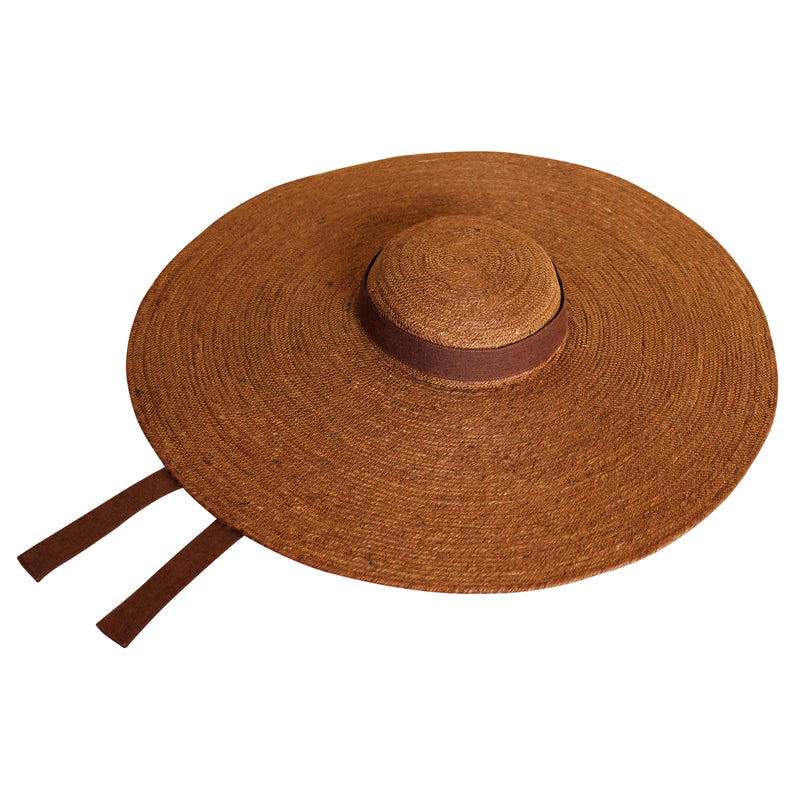 Lola Wide Brim Jute Straw Hat In Havana Brown. Braided meticulously by artisans in Gianyar, Bali from natural Jute material, this sweet hat offers both comfort and elegance. Designed with ideal thickness and weight that allow its brim to be easily folded, stretched, and styled, making it easy to take to any holiday trips or summer vacation.