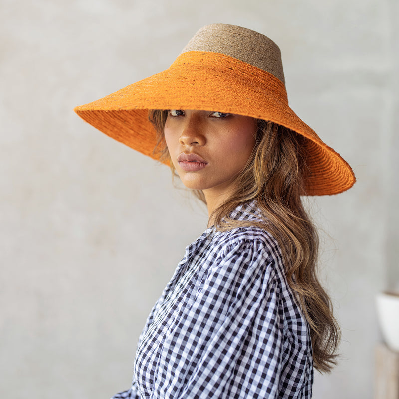 Duo color tone handwoven beach straw hat in natural and pumpkin orange color, handmade from natural jute straw by local artisan in Bali. Handmade vacation wide-brim hat with domed down brim for maximum sun protection. Sustainably made by female artisan community in Indonesia for resort vacation season.