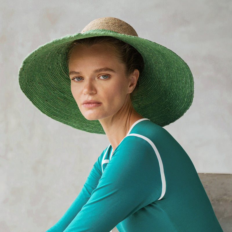 A woman is wearing BrunnaCo Riri Duo Jute hat in Kelly Green & Natural color made by artisans in Bali. This versatile beach hat is a perfect sun hat for a sunny summer day